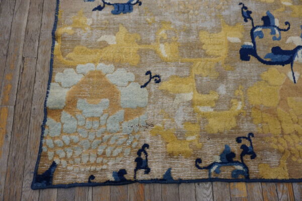 Distressed yellow, light blue, and tan rug corner featuring stylized motifs on gray wood floor.