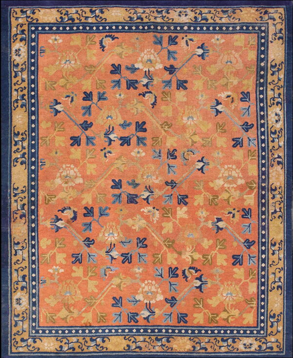 An orange rug with scattered blue and gold stylized floral motifs and a multi-layered navy and gold border.