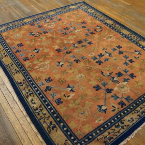 A terra cotta rug with blue and gold floral patterns lies on rustic light brown hardwood flooring.