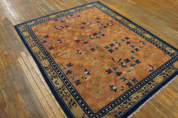 A terra cotta rug with blue and gold floral patterns lies on rustic light brown hardwood flooring.