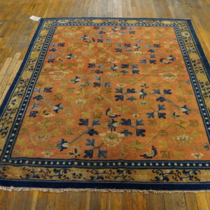 Orange field rug featuring blue and green floral patterns and a wide navy border on distressed wood flooring.