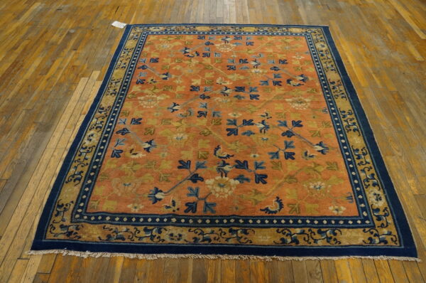 Orange field rug featuring blue and green floral patterns and a wide navy border on distressed wood flooring.
