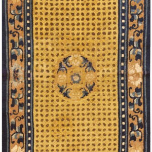 A rectangular rug with a mustard yellow dotted field and dark navy floral borders on a tan ground.