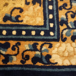 High-pile rug corner in golden yellow with dark blue scrolling vines and a dotted border design.