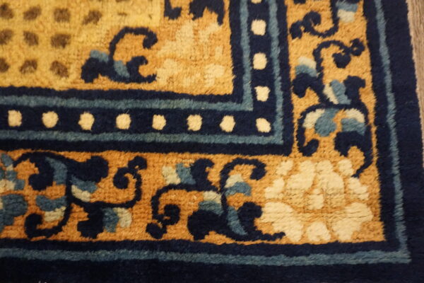 High-pile rug corner in golden yellow with dark blue scrolling vines and a dotted border design.