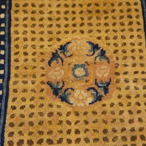 Close-up of a mustard yellow rug field featuring brown dots, a central medallion, and navy blue floral borders.