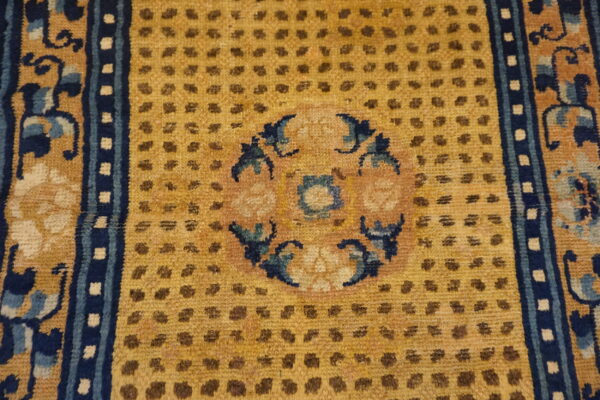 Close-up of a mustard yellow rug field featuring brown dots, a central medallion, and navy blue floral borders.