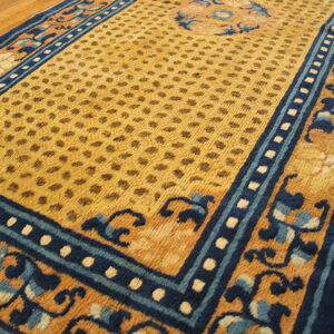 Yellow and blue rug featuring a repeating dot pattern field and ornate scrolling floral borders on hardwood.