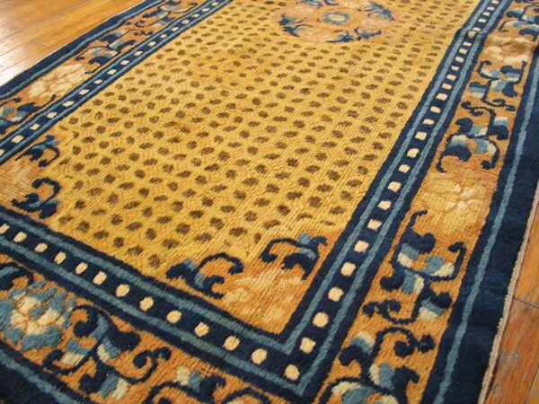 Yellow and blue rug featuring a repeating dot pattern field and ornate scrolling floral borders on hardwood.