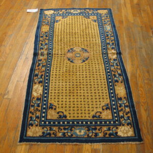 Gold rug with blue floral border and center medallion rests on light brown wood planks.