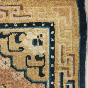 Close-up of a tan, brown, and blue patterned rug corner with visible fringe on a white floor.