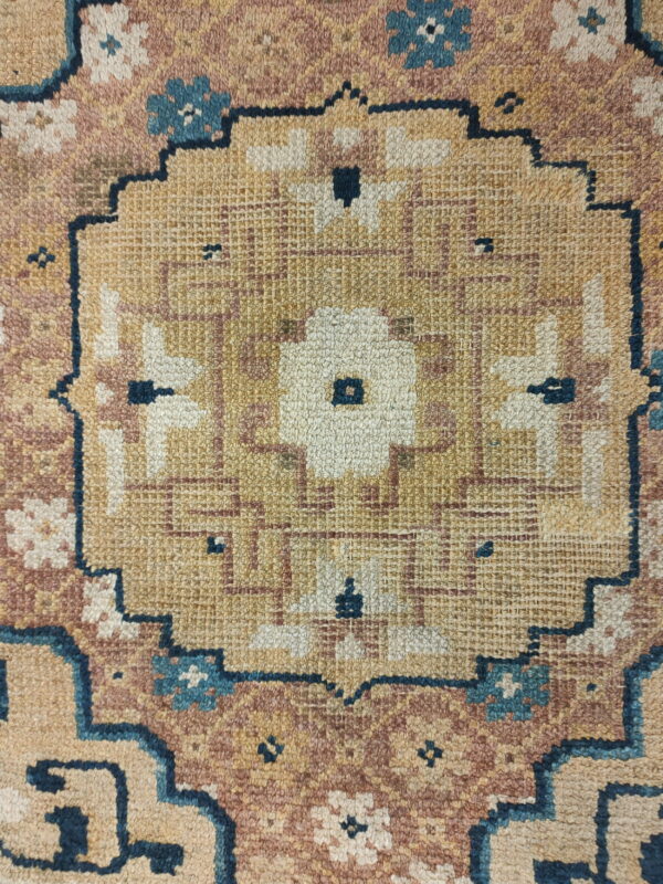 Tan, dusty rose, and cream rug detail with a central medallion and dark blue geometric outlining.