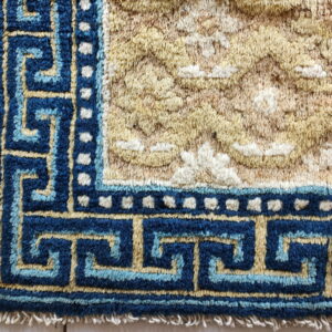 High-pile rug corner with a navy and light blue geometric border and a textured gold and beige field.