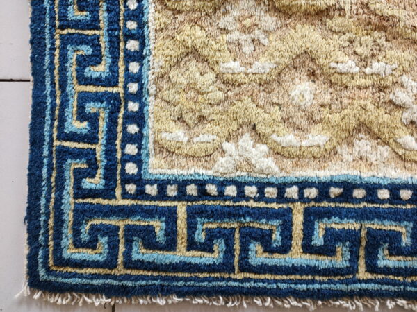 High-pile rug corner with a navy and light blue geometric border and a textured gold and beige field.