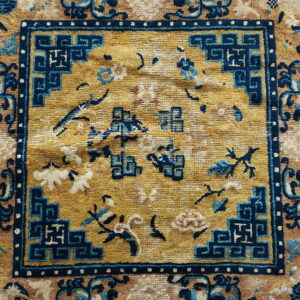 Gold and tan rug detail featuring a navy blue geometric border framing scattered floral motifs.