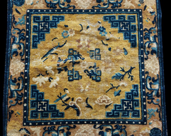 Gold and tan rug detail featuring a navy blue geometric border framing scattered floral motifs.