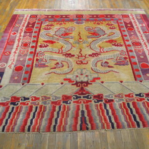 Gold and red rug with twin dragon pattern and graphic borders resting on wide wood planks.