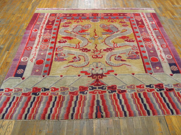 Gold and red rug with twin dragon pattern and graphic borders resting on wide wood planks.