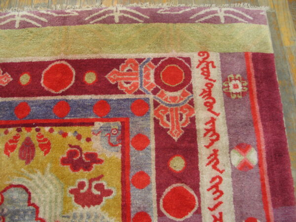 Detailed view of a multi-bordered rug featuring red circles, purple bands, and mustard yellow traditional patterns on wood flooring.