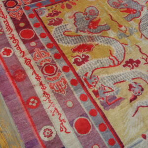 Red and grey dragon pattern on a gold rug field meets a purple and red striped border on wood floor.