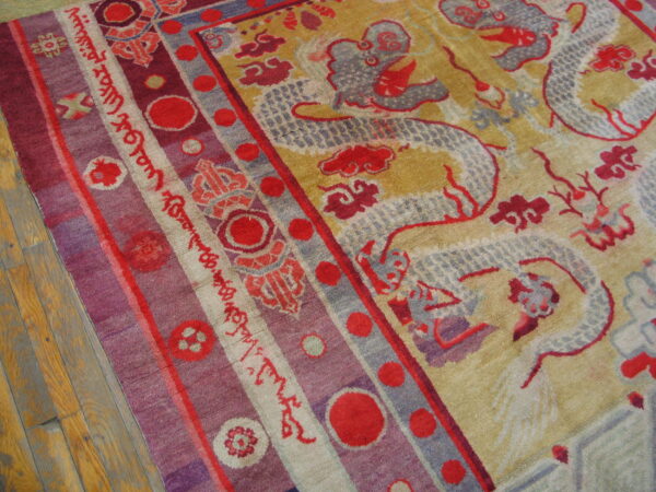 Red and grey dragon pattern on a gold rug field meets a purple and red striped border on wood floor.