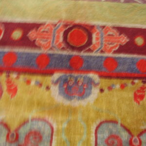 Plush, close-up rug detail showing horizontal stripes, red medallions, and stylized designs on gold.
