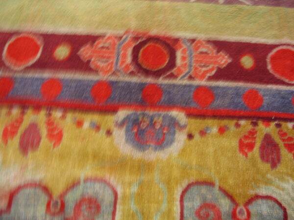 Plush, close-up rug detail showing horizontal stripes, red medallions, and stylized designs on gold.