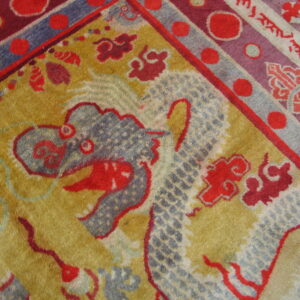 Golden-yellow rug detail featuring a blue-gray dragon motif surrounded by red clouds and a multicolored striped border.