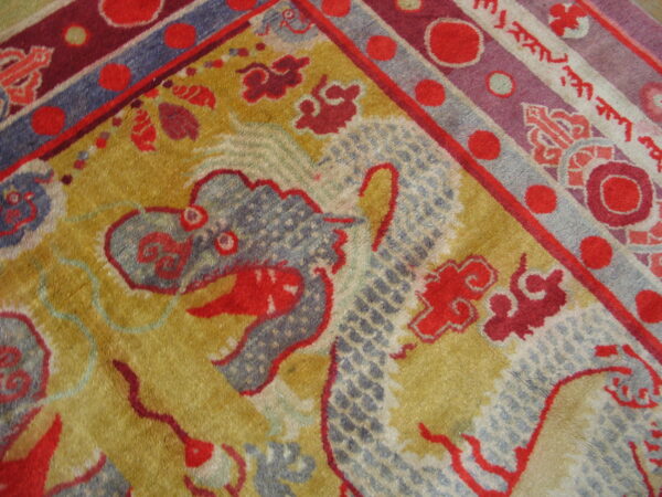 Golden-yellow rug detail featuring a blue-gray dragon motif surrounded by red clouds and a multicolored striped border.