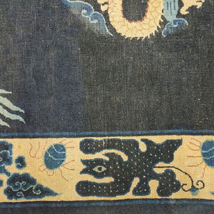 Dark blue patterned rug showing a tan dragon detail and a wide tan border with blue motifs.