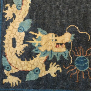 Detailed corner of a high-pile rug showing a cream and blue dragon on a dark blue ground.