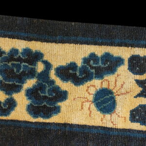 Blue floral and stylized creature motifs decorate the tan border of a dense, low-pile rug.