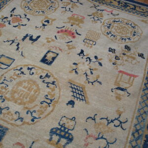 Low-pile beige rug with scattered blue, tan, and coral motifs and a complex dark blue border.
