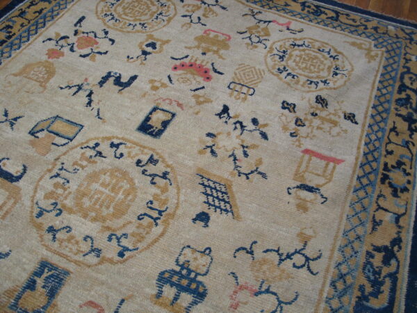 Low-pile beige rug with scattered blue, tan, and coral motifs and a complex dark blue border.