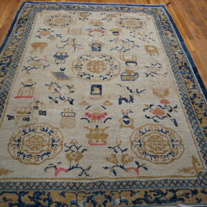 Beige traditional rug with blue, gold, and pink scattered designs and dark blue borders on wood planks.