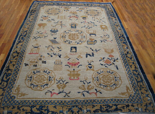 Beige traditional rug with blue, gold, and pink scattered designs and dark blue borders on wood planks.