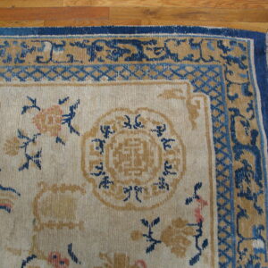 Close-up of a traditional rug featuring a cream field with blue and gold floral motifs on wood flooring.