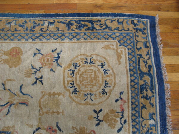 Close-up of a traditional rug featuring a cream field with blue and gold floral motifs on wood flooring.