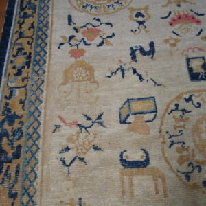 Detail shot of a low-pile rug showing scattered gold and navy motifs on a beige ground with a complex border.