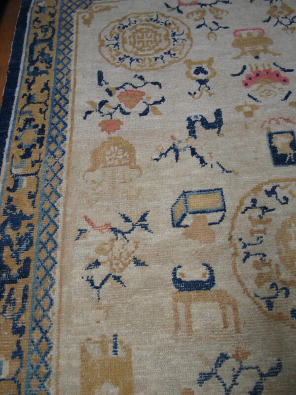 Detail shot of a low-pile rug showing scattered gold and navy motifs on a beige ground with a complex border.