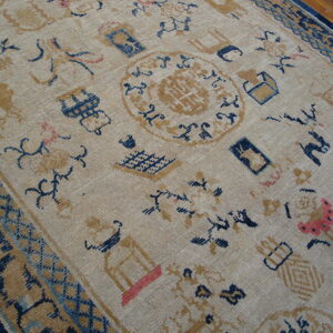Low-pile rug in beige, navy, and gold scattered with symbols, resting on a brown hardwood floor.