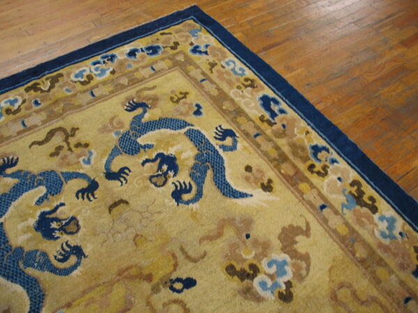 Close-up of a gold rug with blue dragon figures and a navy border on light brown hardwood floors.