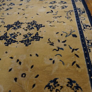 A large golden rug featuring navy blue traditional patterns and borders rests on hardwood floors.