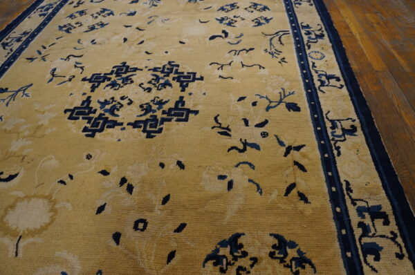 A large golden rug featuring navy blue traditional patterns and borders rests on hardwood floors.