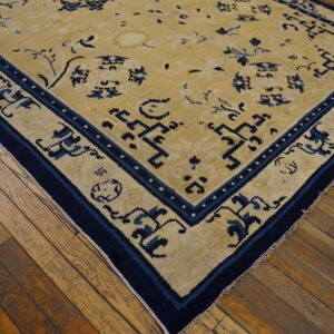 A pale yellow rug with dark blue traditional floral and geometric patterns rests on worn wood flooring.