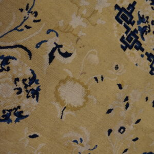 Yellow rug close-up showing blue and cream floral patterns and a dark blue geometric border section.
