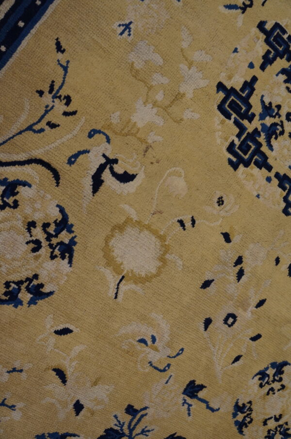 Yellow rug close-up showing blue and cream floral patterns and a dark blue geometric border section.