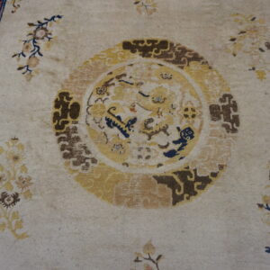 Low-pile beige rug with gold central medallion, scattered florals, and a bold navy blue key pattern border.