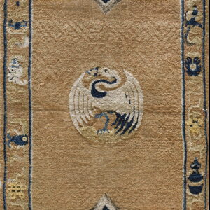 Tan high-pile rug detail showing a white bird medallion and stylized blue and yellow geometric borders.