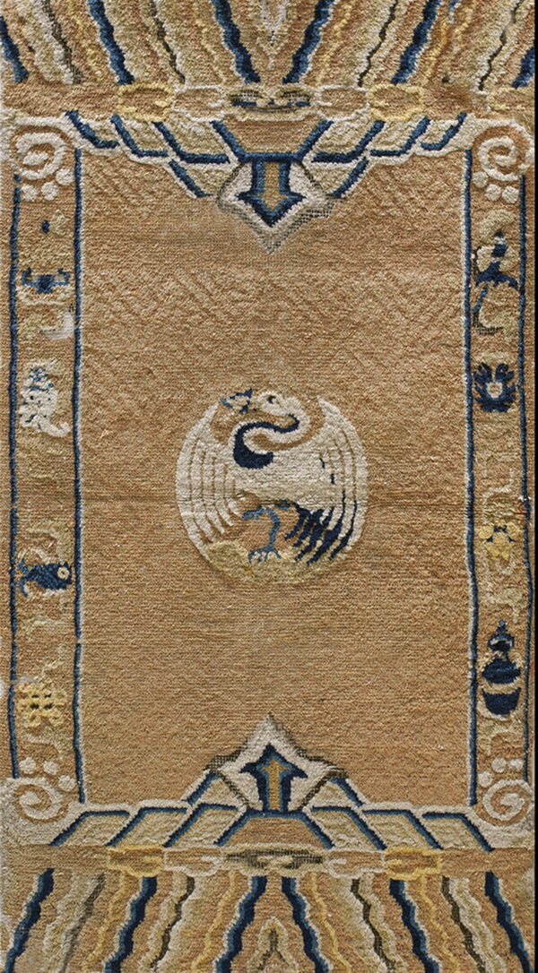Tan high-pile rug detail showing a white bird medallion and stylized blue and yellow geometric borders.